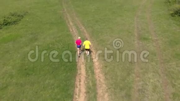 高级跑步者和他的成年儿子在草地路跑步空中镜头视频的预览图