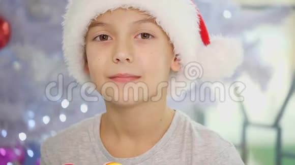 一个穿着圣诞帽的滑稽男孩穿着睡衣坐在床上展示条纹糖果罐头的视频视频的预览图