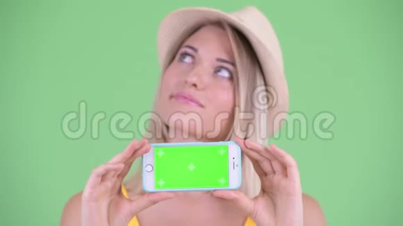 一位年轻的金发美女一边看着电话一边思考着视频的预览图