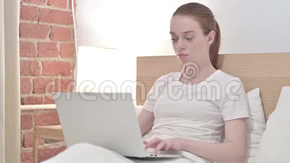 疲惫的红头发年轻女子在床上背痛视频的预览图