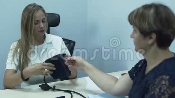 漂亮的白种人医生测量一位坐在办公室桌子旁的老年妇女的压力成熟的女人视频的预览图