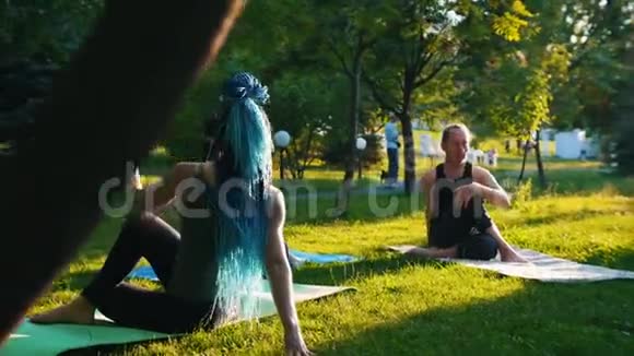 两位年轻女性在公园里和教练一起做不同的瑜伽练习一位女性长着蓝色的恐惧症视频的预览图