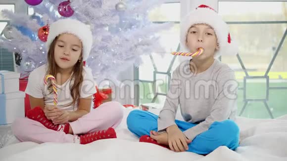 可爱的白种人孩子们享受圣诞节的早晨在床上玩耍品尝糖果罐并把它们扭在手中男孩是视频的预览图