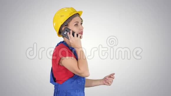漂亮的年轻建筑工女戴着黄色的安全帽在梯度背景上打电话视频的预览图