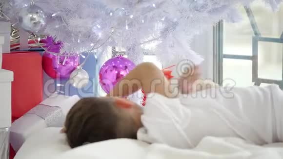 幼儿躺在圣诞树下摸着球看着他在粉红色玻璃球中的倒影的视频视频的预览图