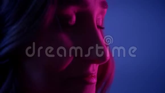 近景拍摄年轻漂亮的女性脸在镜头前带着霓虹蓝背景开心地微笑视频的预览图