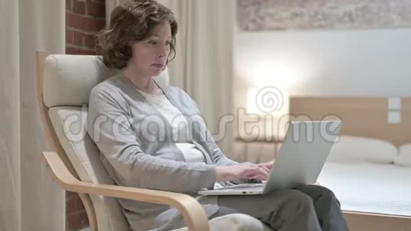 惊喜的老妇人在沙发上用笔记本电脑庆祝成功视频的预览图
