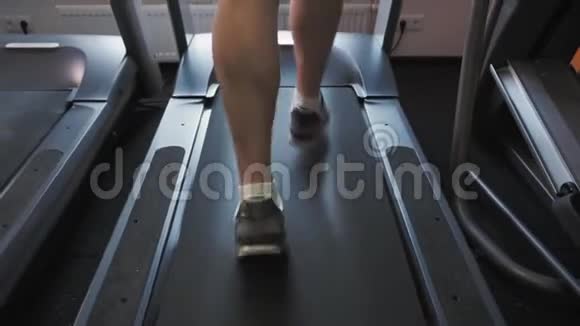 在健身室的跑步机上奔跑的无法辨认的男人的腿关闭背部低角度拍摄视频的预览图