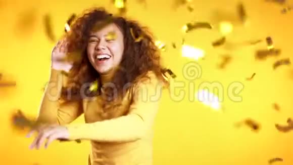 兴奋的女孩跳舞鼓掌为黄色工作室里的纸屑雨而高兴视频的预览图