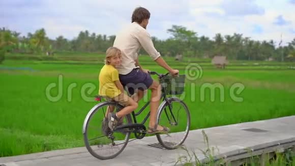 一个年轻人和他的小儿子骑着自行车穿过美丽的稻田前往东南亚构想视频的预览图