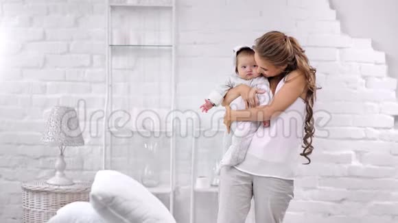 幸福的家庭迷人的年轻母亲和可爱的宝宝在白色舒适的内部度过美好的时光视频的预览图