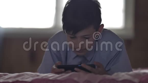 有趣的男孩晚上躺在床上用电话视频的预览图