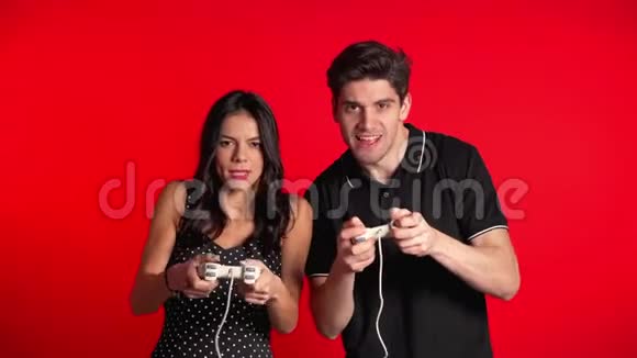 漂亮的年轻夫妇在TV上玩电子游戏红色工作室墙上有操纵杆利用现代技术视频的预览图