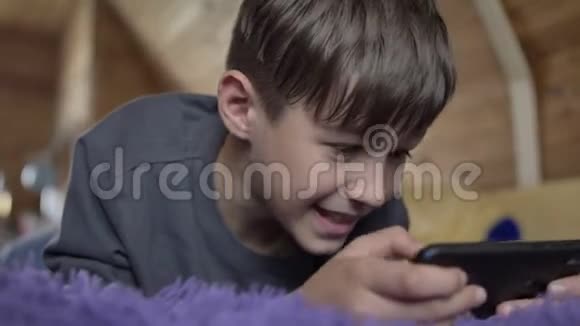 有趣的男孩躺在床上玩电话游戏视频的预览图