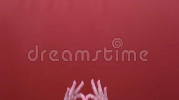 女性通过在红色工作室背景下的手摆姿势制作标志心形视频的预览图