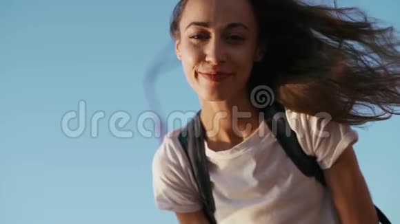 快乐的微笑着穿着白色t恤的年轻漂亮女人站在蓝天背景上的桥上笑着视频的预览图