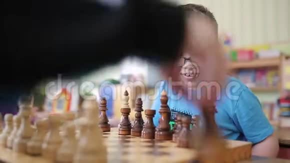 一个戴眼镜的男孩下棋他坐在桌子旁玩着情绪激动地笑着他想和他的同伴视频的预览图