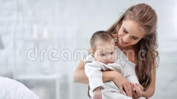 可爱的妈妈微笑着亲吻可爱的孩子在白色的室内休息视频的预览图