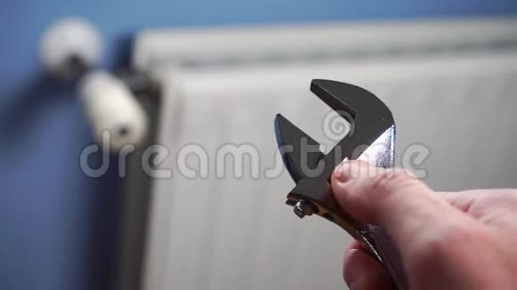 蓝色墙壁上白色暖气片背景上男性修理工手中的可调扳手视频的预览图