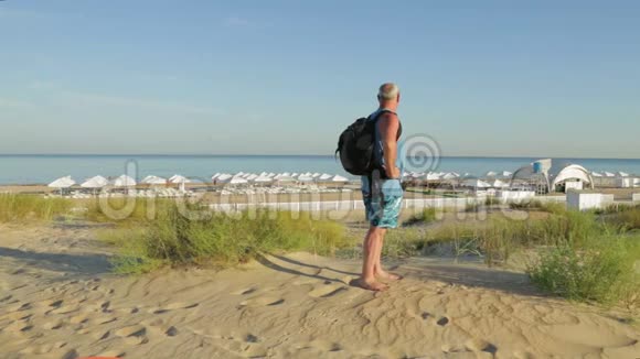 一个带着赤脚背包的人正在海边的背景下赤脚行走视频的预览图