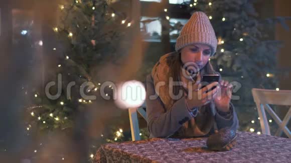 冬天女人坐在户外咖啡馆的露台上在社交网络上聊天用智能手机和圣诞节视频的预览图