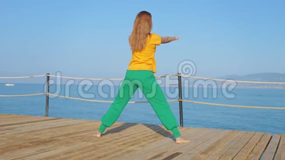 年轻女子在海上或海洋的背景下在木墩上做伸展运动视频的预览图