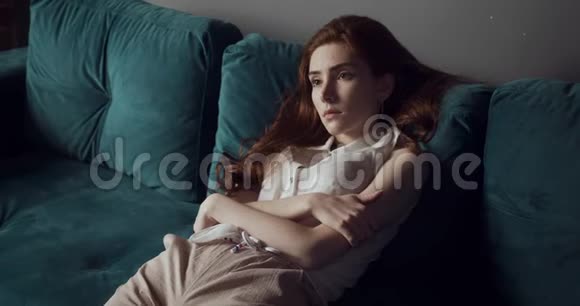 年轻疲惫的女人坐在家里的蓝色沙发上视频的预览图