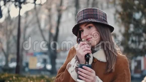 一个戴着帽子的黑发美女正在喝咖啡在一条城市街道上摆姿势视频的预览图
