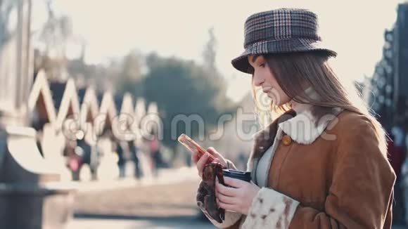 一个戴着帽子的漂亮黑发女人正在城市街道上喝一杯外卖咖啡视频的预览图