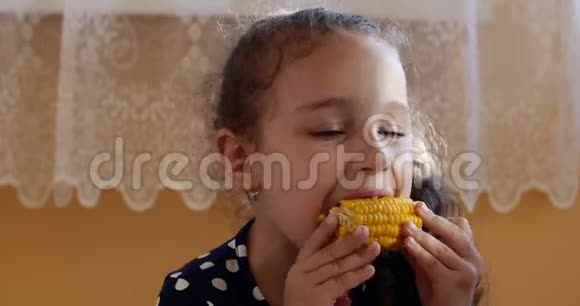 可爱的小女孩在温暖的夏天享受美味的玉米孩子在家吃煮玉米看着相机视频的预览图