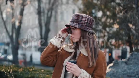一个戴着帽子的黑发美女正在喝咖啡在一条城市街道上摆姿势视频的预览图