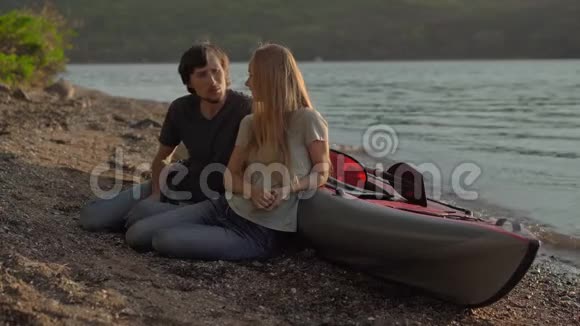 一群年轻的男女游客坐在海边或湖边的一艘充气大皮艇旁视频的预览图