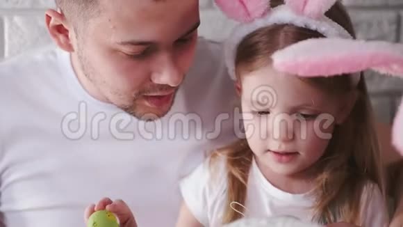 父亲和他的小女儿正在用刷子把复活节彩蛋涂成彩色视频的预览图