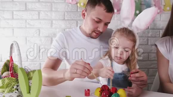 父亲和他的小女儿正在用刷子把复活节彩蛋涂成彩色视频的预览图