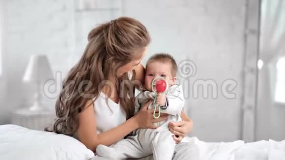美丽的妈妈在晨白的卧室里摇摆着微笑的可爱的宝宝视频的预览图