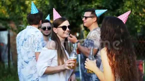 两个快乐的女人在夏天的聚会上聊天喝啤酒男人在后台戴着节日帽视频的预览图