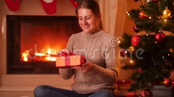 4k视频年轻女子坐在圣诞树和壁炉旁的地板上打开圣诞礼盒视频的预览图