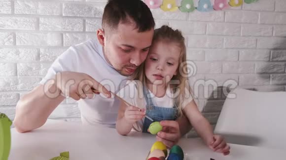 父亲和他的小女儿正在用刷子把复活节彩蛋涂成颜色视频的预览图