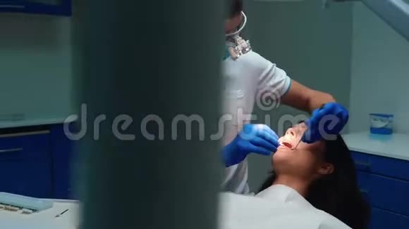 年轻牙医戴着医用手套口罩和眼镜用牙镜和牙坝病人的牙齿视频的预览图