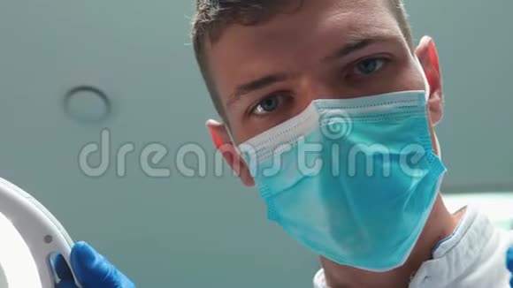 戴口罩的年轻英俊医生牙科医生在病人检查时借助牙科镜手持医疗灯视频的预览图