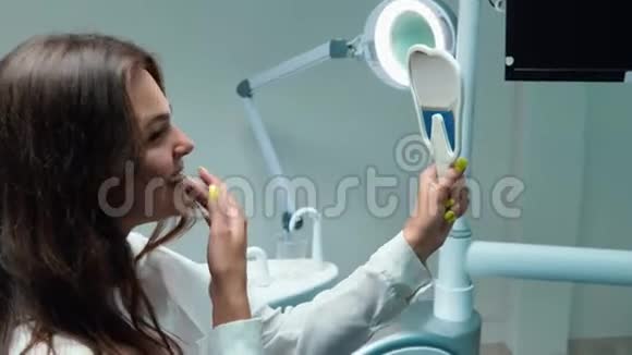 年轻漂亮的黑发女人的病人看起来很开心因为她坐在牙医看着镜子视频的预览图