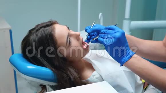年轻英俊的牙医戴着蓝色的手套口罩和眼镜用牙镜牙坝来治疗病人的牙齿视频的预览图