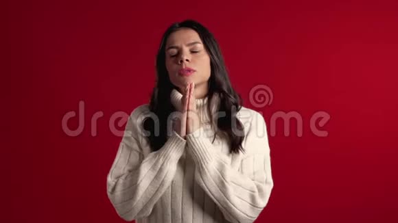 可爱的拉丁女孩穿着温暖的白色毛衣在红色背景下祈祷女人求人4k视频的预览图