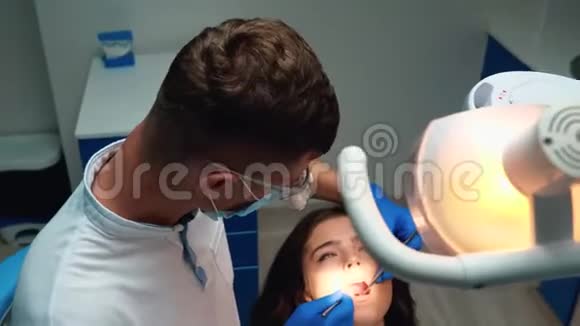 戴医疗手套口罩及眼镜的年轻牙医并使用牙科镜及牙科镜治疗病人的牙齿视频的预览图