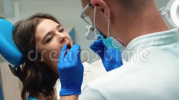戴眼镜的年轻牙医检查年轻的黑发女人病人使用牙齿的问题视频的预览图
