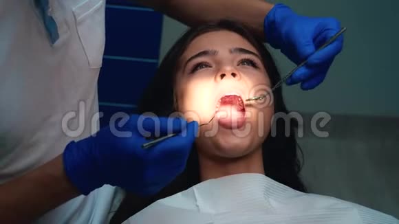 戴医疗手套和口罩的牙医在预约牙科时使用牙科镜和牙坝治疗病人牙齿视频的预览图
