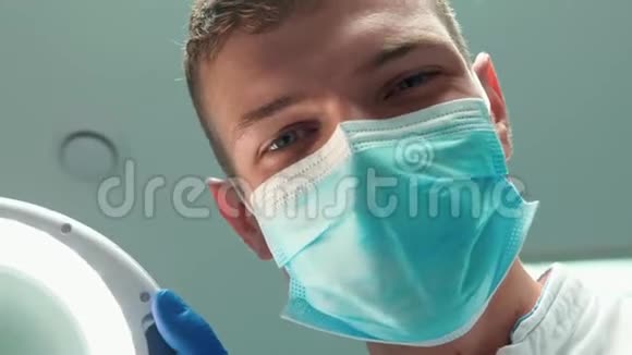年轻英俊的微笑医生戴口罩的牙科医生借助牙科镜在病人检查时手持医疗灯视频的预览图