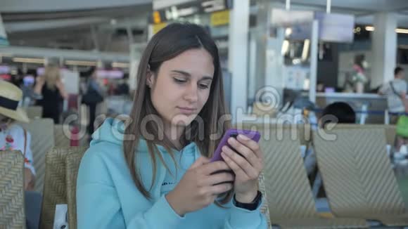年轻女子正在机场等她的飞行女性点击智能手机4k视频的预览图