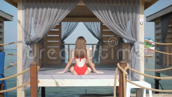 阳光明媚的假期年轻女子穿着泳衣美丽的身体放松在海边的一个昂贵的度假胜地的平房视频的预览图