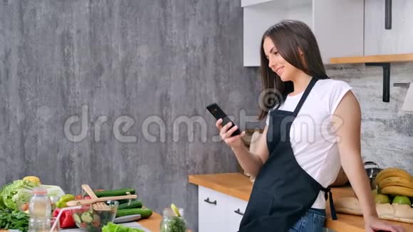 微笑的家庭主妇用智能手机聊天在厨房烹饪美味的健康食物视频的预览图